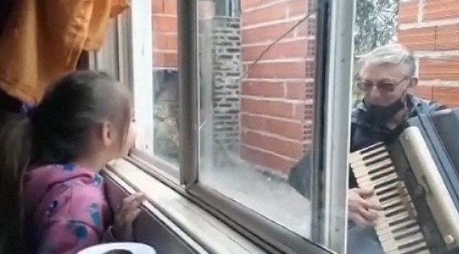 Vecino toca el acordeón desde la ventana para acompañar a su familia que tiene covid
